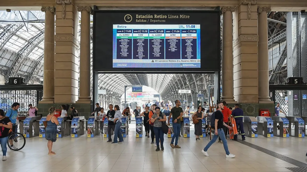 Estación de trenes llena de gente con una pantalla con avisos de horarios de llegada del transporte.