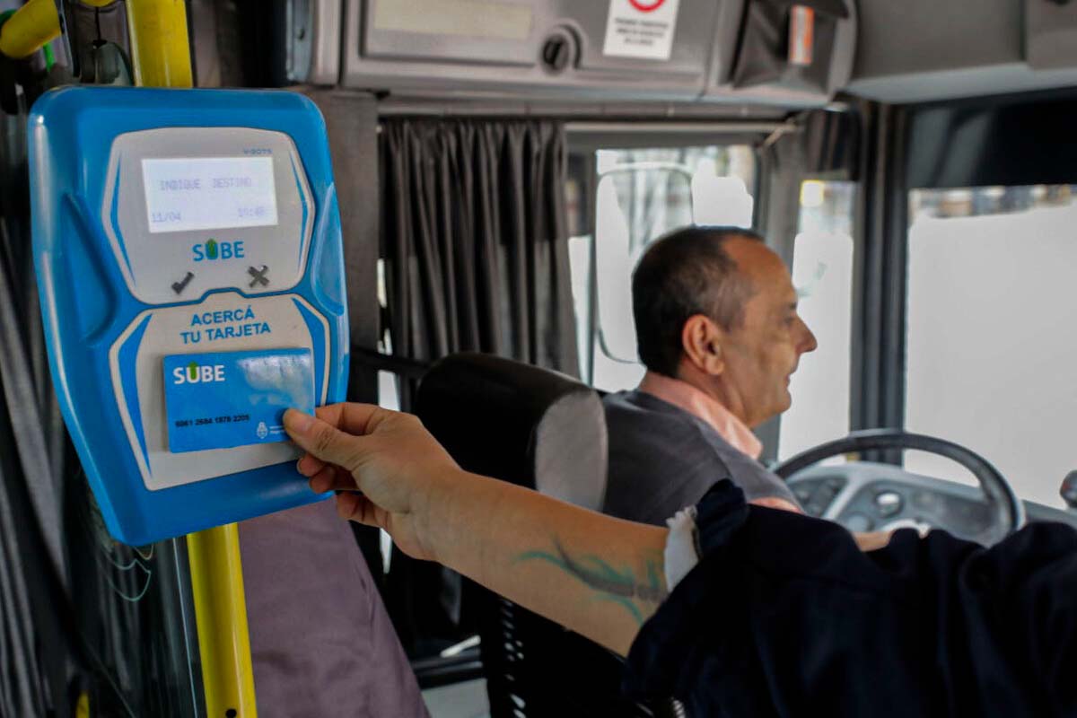 Una persona apoyando la tarjeta SUBE sobre el lector dentro de un colectivo mientras se ve al conductor de espaldas.