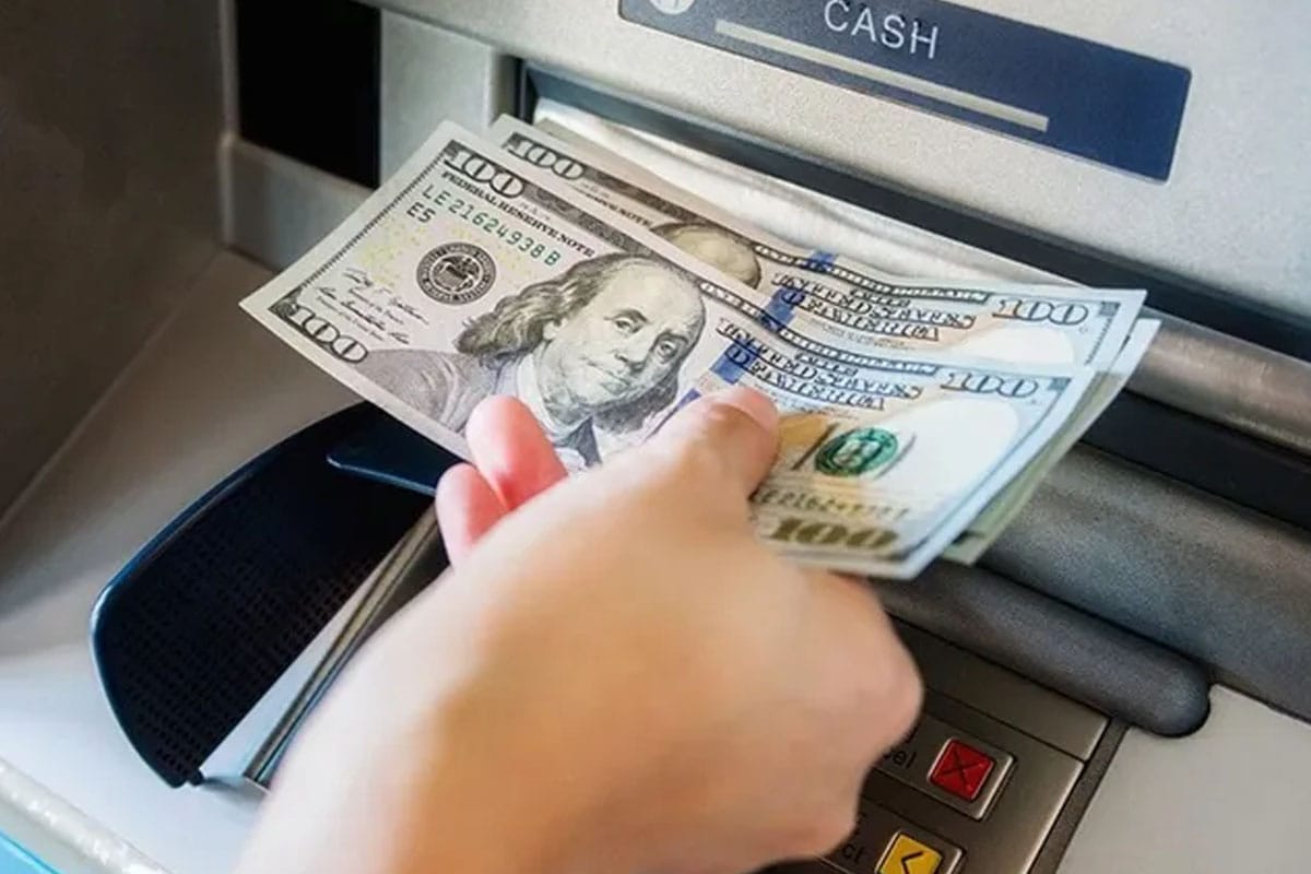 Imagen de una persona retirando dólares de un cajero automático.